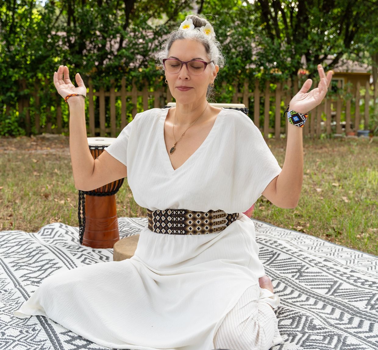Woman meditating outdoors on a patterned blanket.