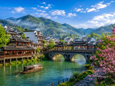 Scenic river with traditional architecture and mountains.