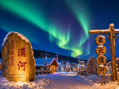 Northern lights over a snowy village entrance with Chinese inscriptions.