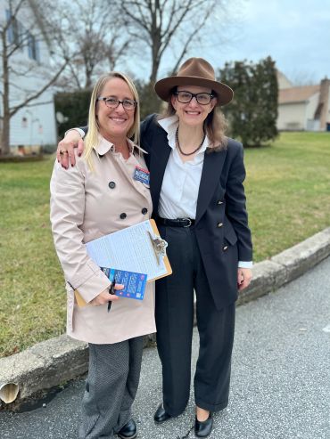 Two smiling women standing outdoors on pavement.