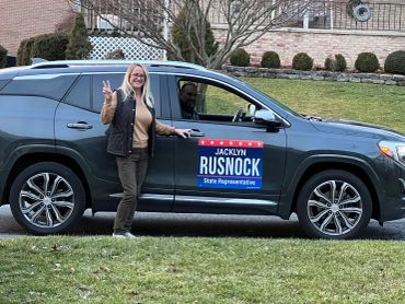 Woman posing with a car displaying a political campaign sign.