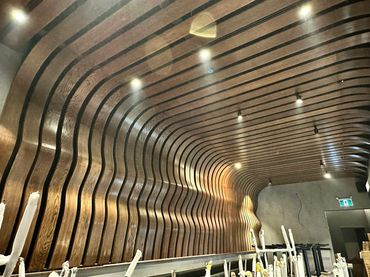 Curved wooden slats form a wavy ceiling design with recessed lights.