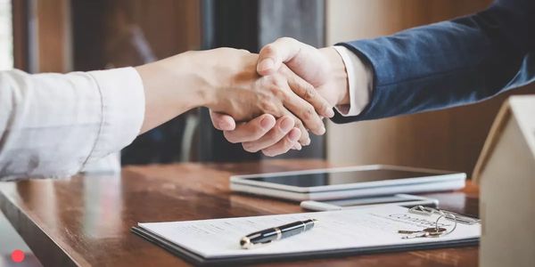 Two people shaking hands over a contract on a wooden table.
