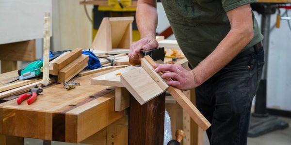 A person using a hand plane to smooth a wooden piece in a workshop.