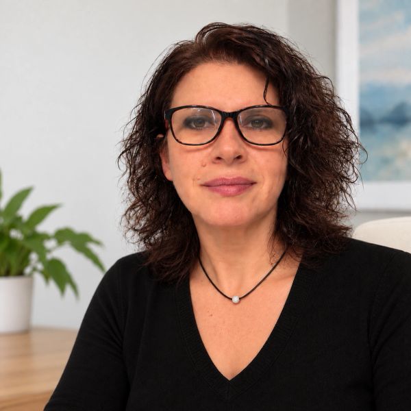 Woman with curly hair and glasses, wearing a black top.