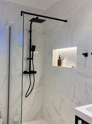 Modern black shower fixtures in a white marble-tiled bathroom.