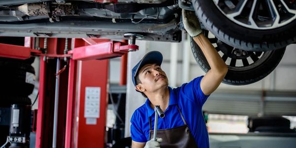 Mechanic inspecting and working on a car's undercarriage in a garage.