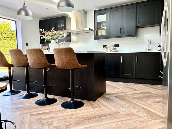Modern kitchen with black cabinets, brown bar stools, and chevron wood flooring.