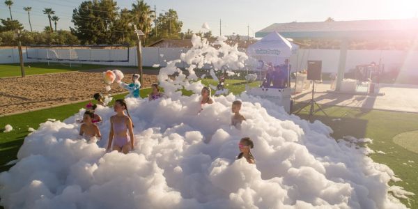 Kids playing in a large foam pit outdoors under sunlight.