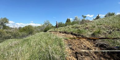 A person stands on a grassy hill beside a dirt trail under a bright blue sky.