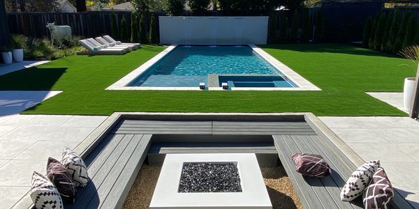 Modern backyard with pool, sun loungers, and sunken seating area with fire pit.