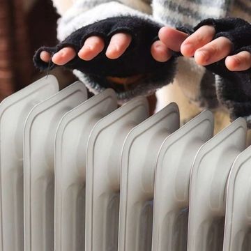 Hands in fingerless gloves warming by a heater.