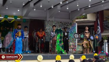 A group of performers in colorful costumes on stage during a cultural event.