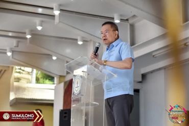 A man in a blue shirt speaking at a podium indoors.