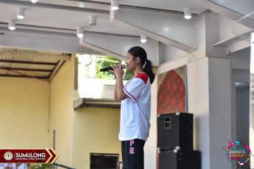 A young girl speaks into a microphone on stage at a school event.