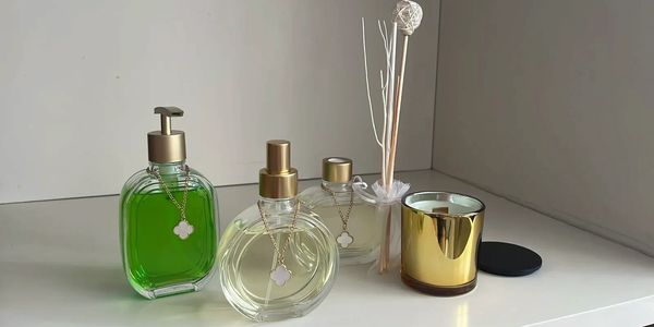 Elegant green and clear glass bottles with golden caps and a gold candle on a white surface.