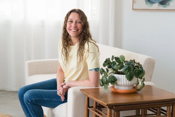 Woman smiling while sitting on a beige armchair indoors.