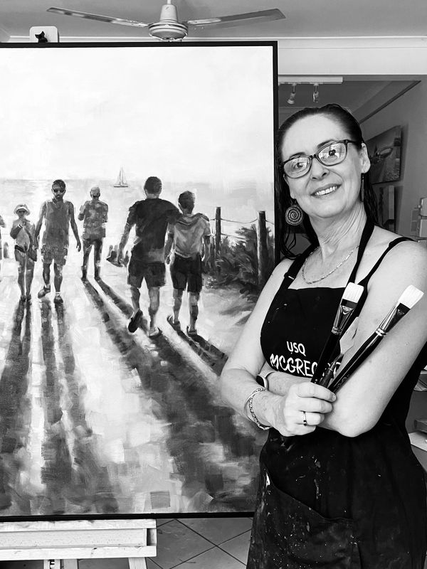 Artist posing with brushes beside her painting of people walking at sunset.