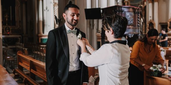 A man in a tuxedo having a boutonniere pinned on in a church.
