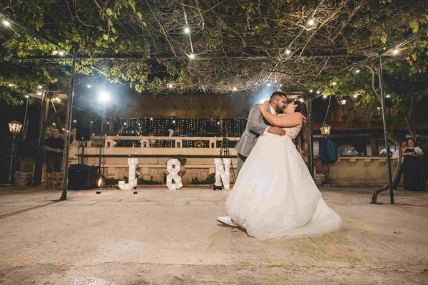 Newlyweds share a romantic dance under string lights with initials J &amp; N glowing behind them.