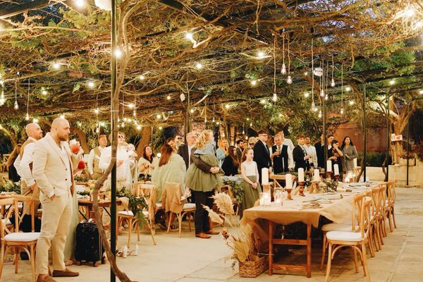 Guests standing under string lights at an outdoor rustic wedding reception.