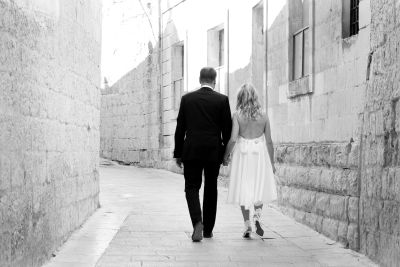 Couple in formal attire walking hand in hand down an alley.