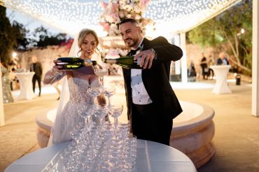 Bride and groom pouring champagne into a pyramid of glasses at their wedding.