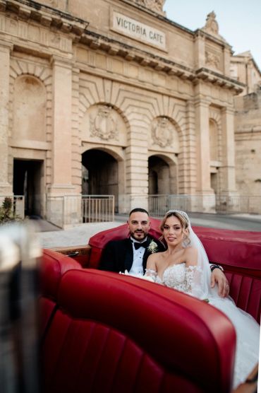 Newlywed couple in a red vintage car near Victoria Gate.
