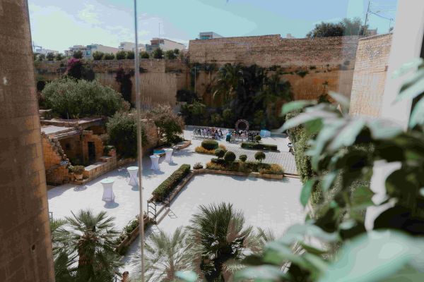 A sunny courtyard with palm trees and seating areas, surrounded by tall walls.