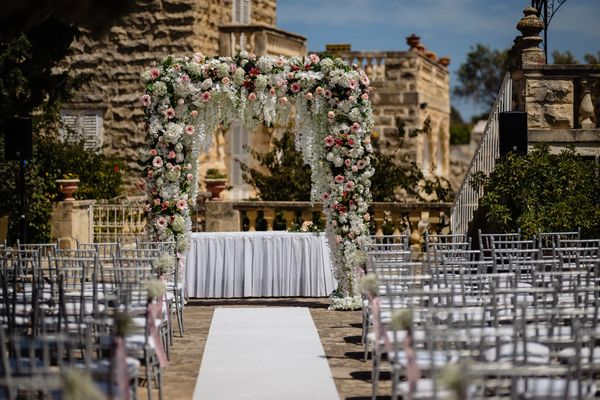 Elegant floral arch at a wedding ceremony in a historic stone courtyard.