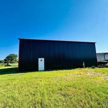 Black metal building with white door on grassy field under blue sky.