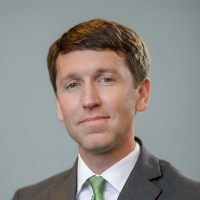 Professional man in suit with green tie against gray background.