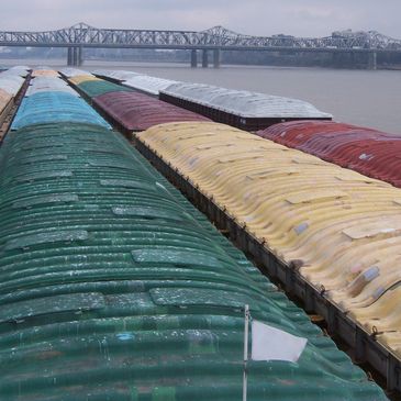 Colorful covered barges on a river with a bridge in the background.