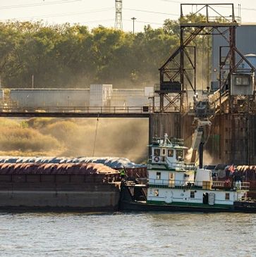 A tugboat pushing a barge loaded with cargo near an industrial dock.