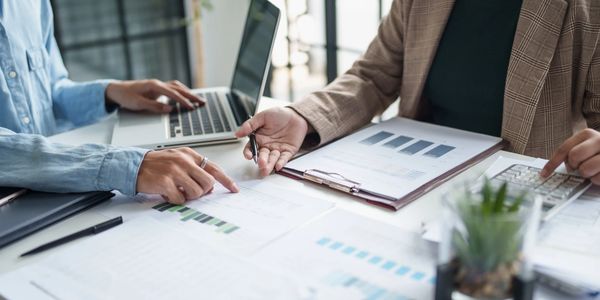 Two professionals discussing charts and data with a laptop and calculator on the desk.