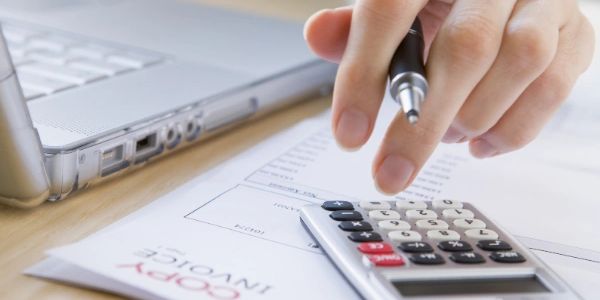 Person using a calculator and pen near a laptop on an invoice.