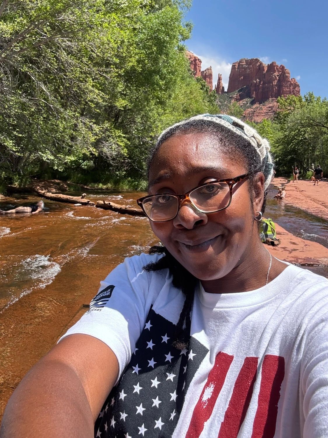 Woman taking a selfie near a scenic river with red rock formations.