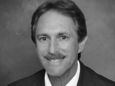 Black and white headshot of a smiling man with a mustache.