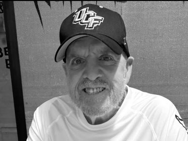 An elderly man wearing a UCF cap and white shirt.