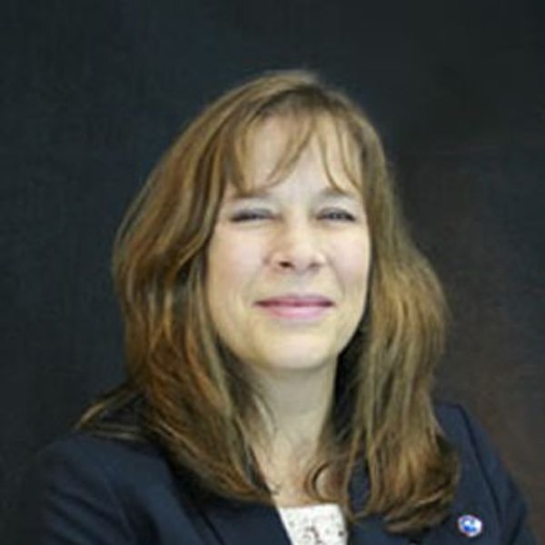 Woman with light brown hair smiling slightly, wearing a dark blazer.