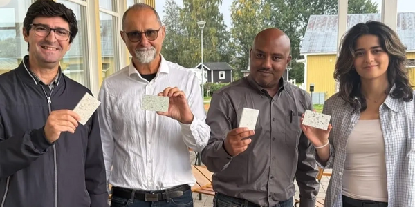 Four people holding rectangular samples, standing outside near a building.