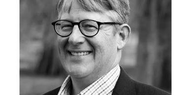 Smiling man with glasses in a black and white portrait.