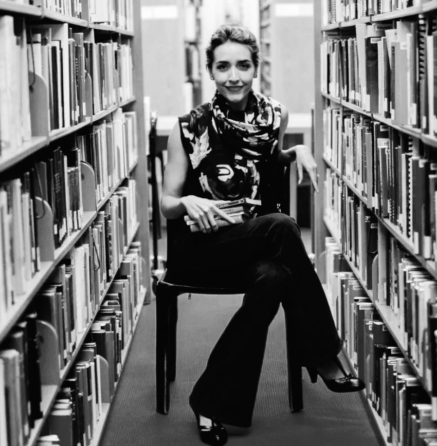 Photo by Ivan Pierre Aguirre featuring the author sitting in between two rows fulls of book.