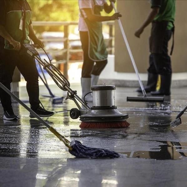 Workers cleaning a floor using various cleaning tools including a floor scrubber and mops.