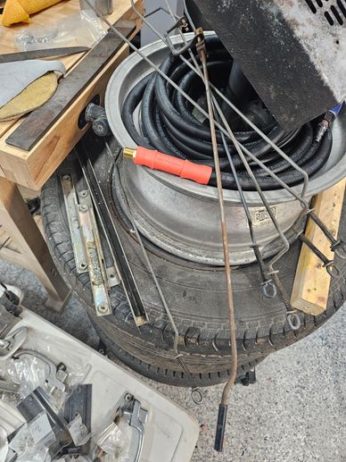 A cluttered workspace with tools, cables, and a tire wheel.