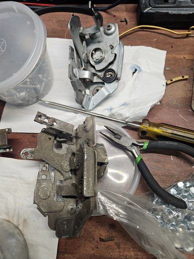 Two metal latch mechanisms and tools on a wooden workbench.