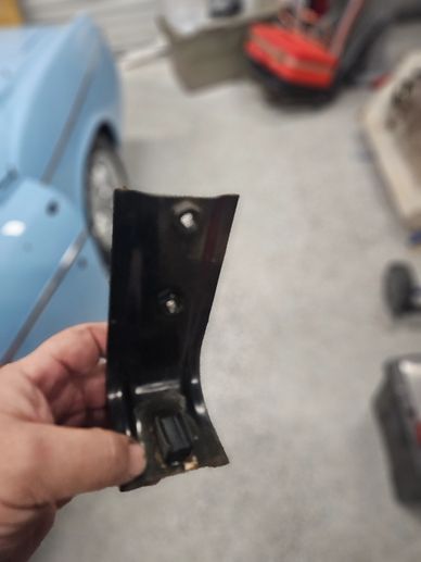 Hand holding a small black metal car part in a garage.