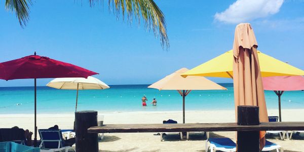 Colorful beach umbrellas and loungers on a sunny tropical beach with clear blue water.