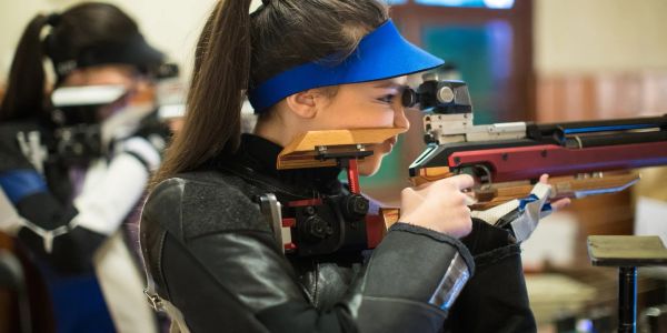 Female shooter aiming with air rifle indoors.