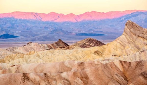 Sunset casts pink hues over desert mountains with rocky ridges and valleys.